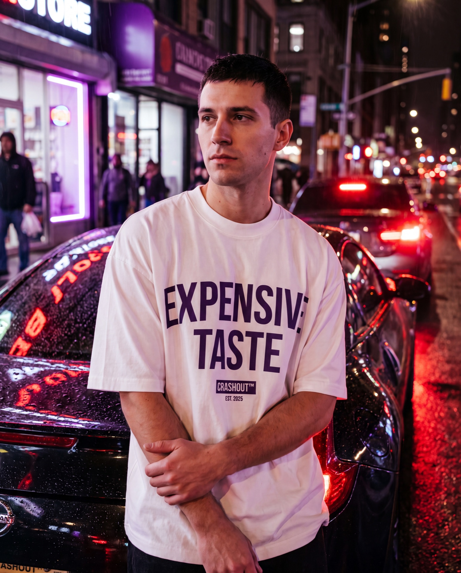 Model leaning on a car at night, red taillights, wearing an Expensive Taste tee